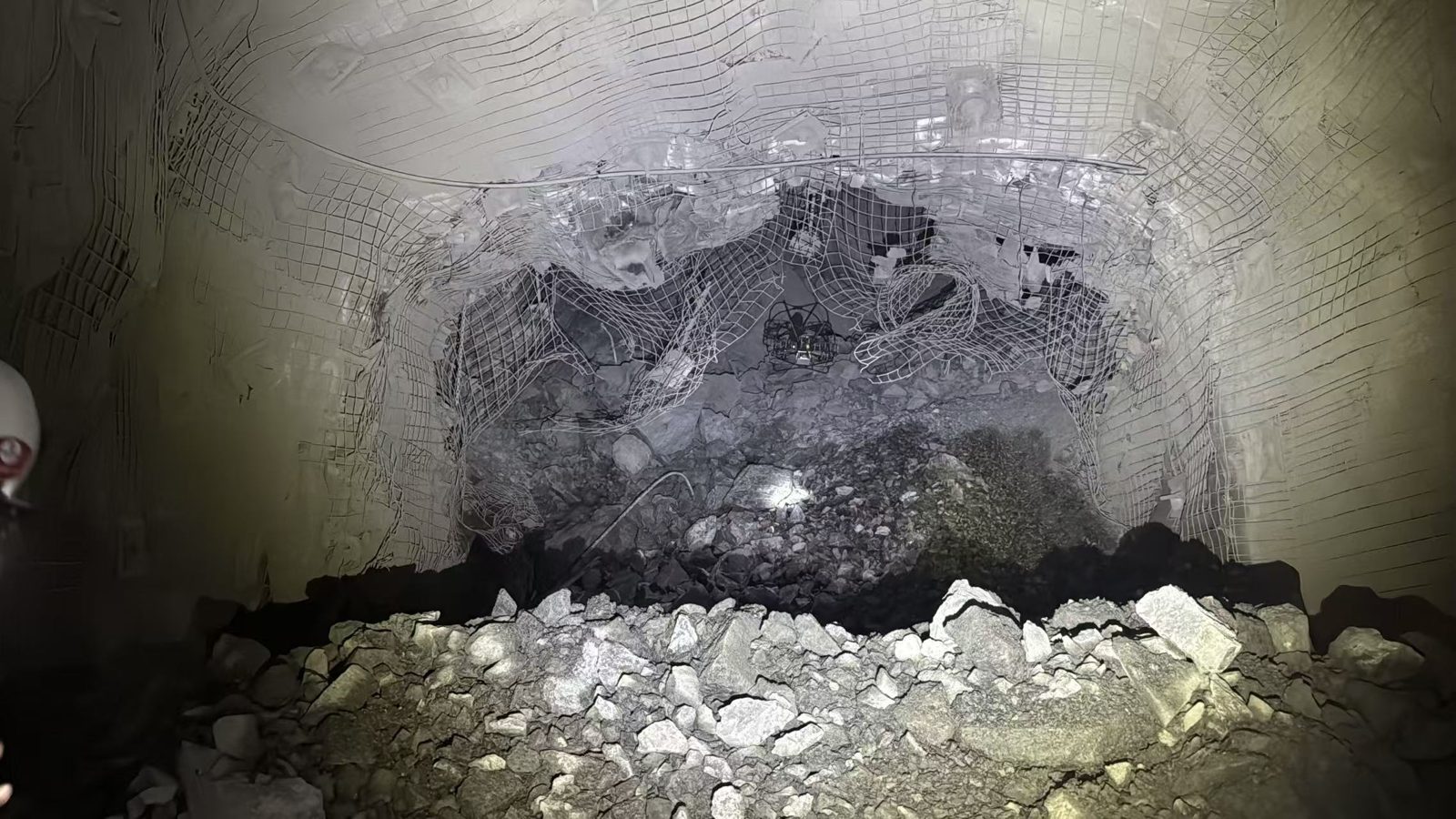Rock face underground covered in mesh, with loose rubble piled at its base